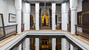A multi-level interior with white columns, a central staircase, and a balcony with ornate railings. - Riad Olema et Spa (Marrakech)