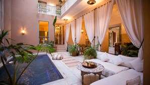 A luxurious indoor pool area with a white sofa, a small round table, and a staircase leading to an upper level. - Riad Olema et Spa (Marrakech)