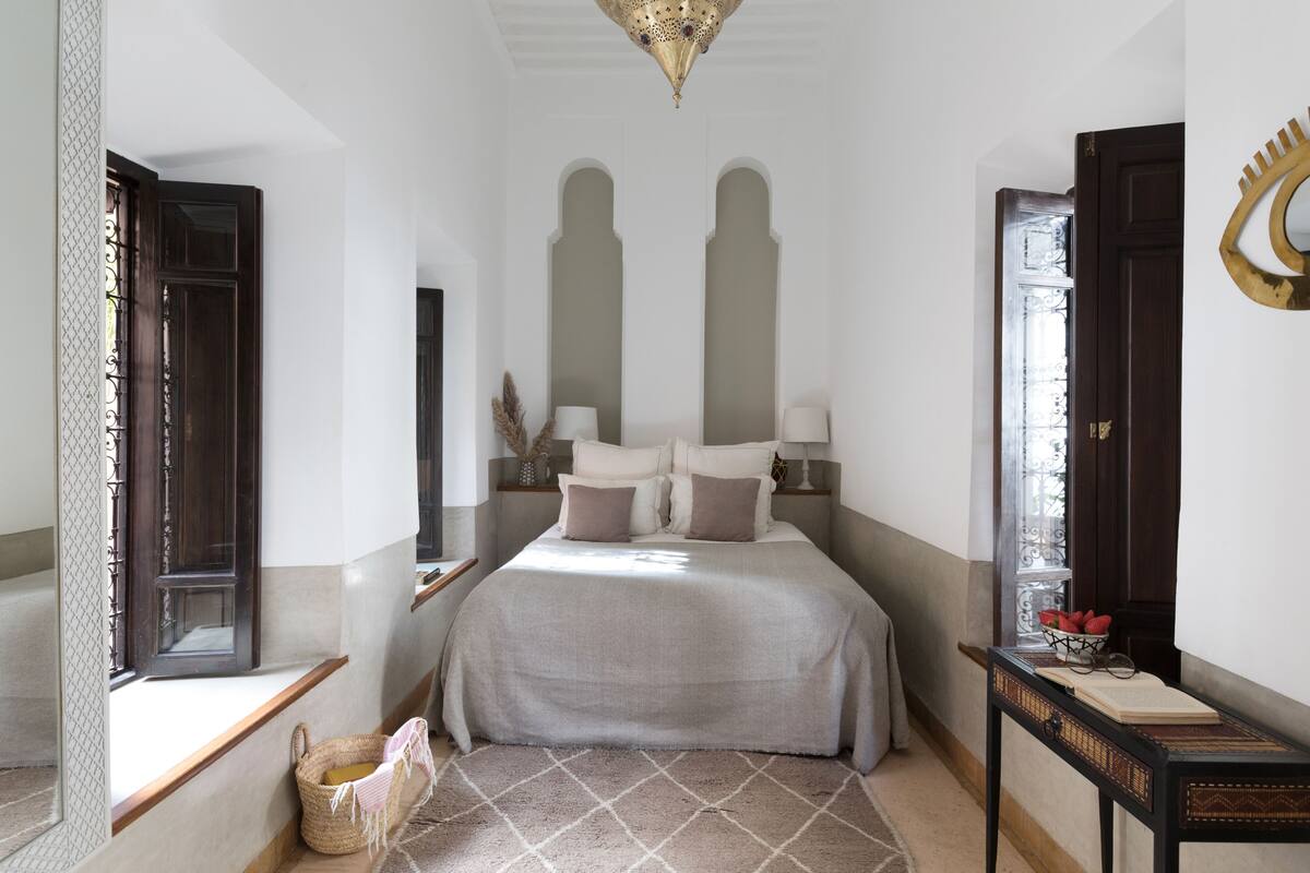 Un dormitorio con cama, mesitas de noche, ventana y puerta.