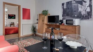 Ein modernes Wohnzimmer mit einer Couch, einem Esstisch mit Weingläsern, einem Fernseher, einer Mikrowelle und einem Vintage-Poster an der Wand.
