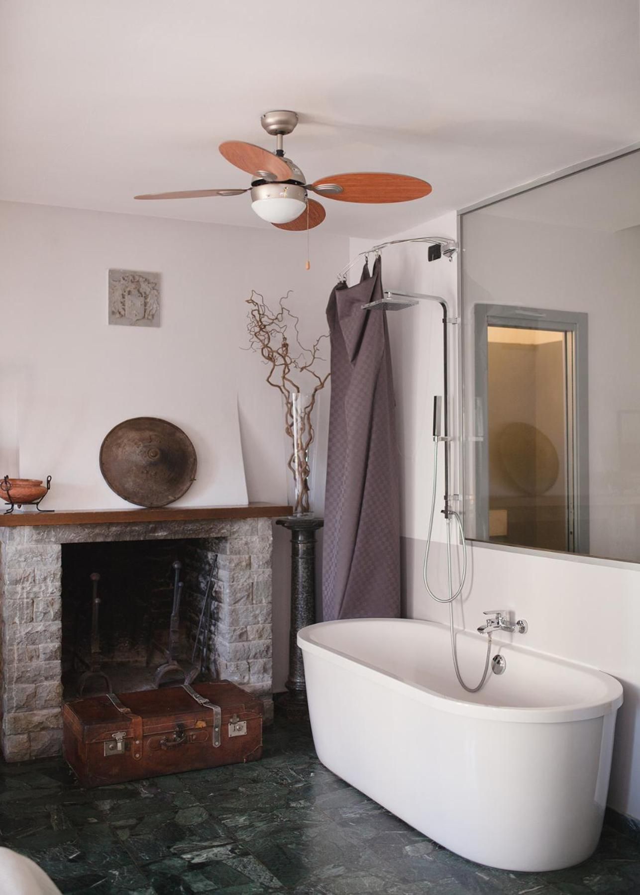 Une salle de bain avec une baignoire sur pieds, une douche, un ventilateur de plafond et une cheminée.