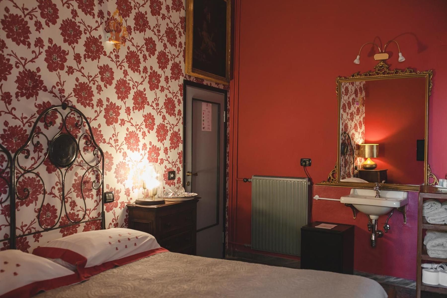 A bedroom with a bed, a bedside table with a lamp, a radiator, a mirror, and a shelf with towels.