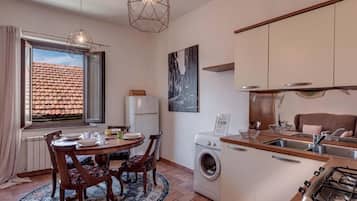 A compact kitchen with a washing machine, a dining area with a table and chairs, and a window with a view of a tiled roof.