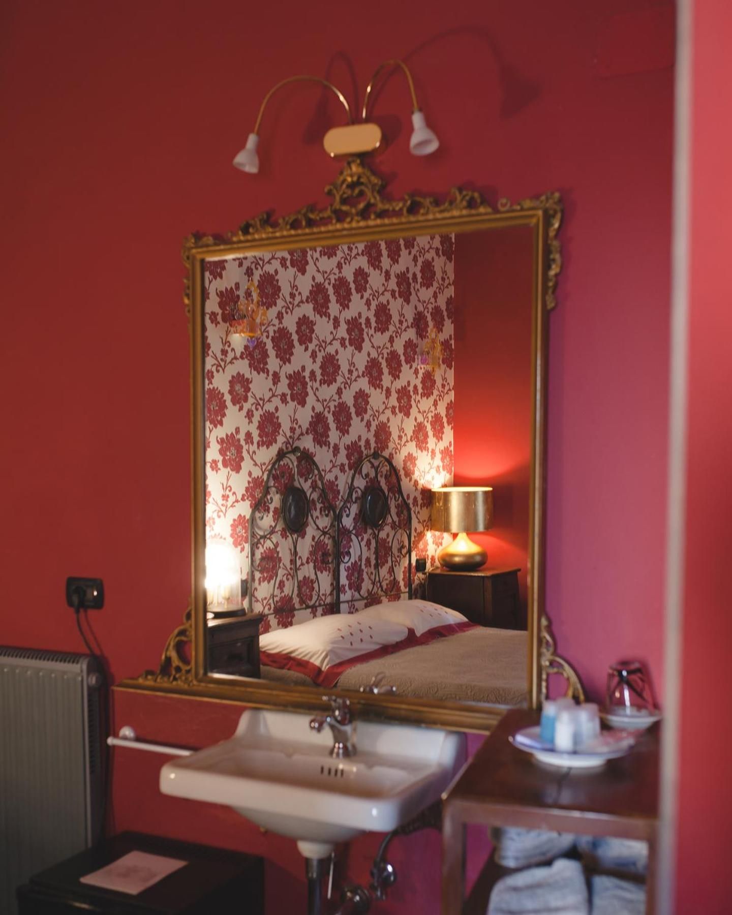 A bedroom with a large mirror, a bedside lamp, a radiator, and a sink.