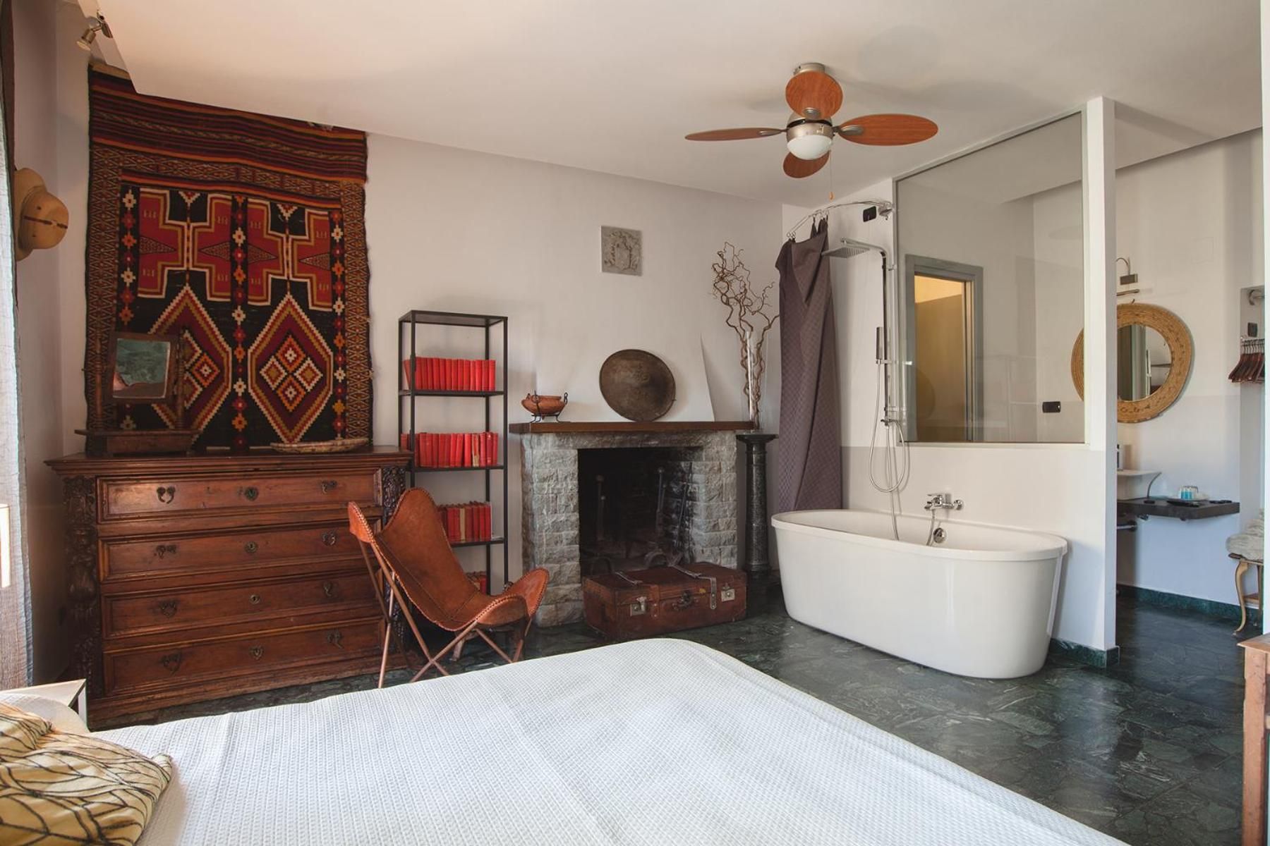 A bedroom with a bed, a dresser, a bookshelf, a fireplace, a bathtub, and a ceiling fan.