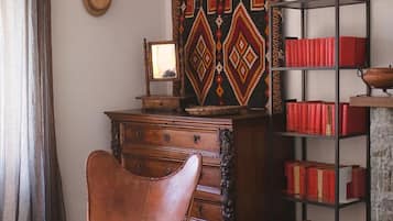 Una habitación con un aparador de madera, un sillón de cuero, una estantería con libros rojos y un tapiz decorado.