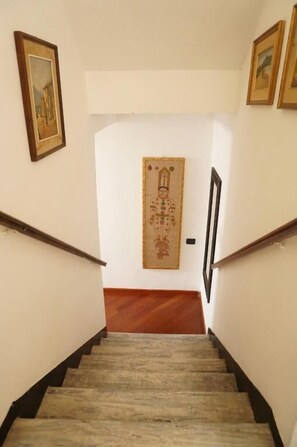 A staircase with wooden steps and black handrails, leading to a door with a decorative panel. - Scarlino Ospitalità Diffusa (Scarlino)