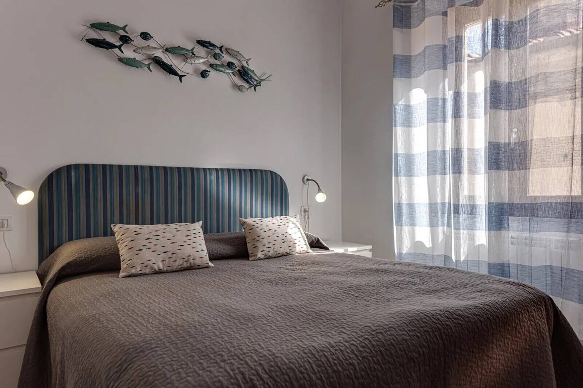 Un dormitorio con cabecera a rayas, dos lámparas de noche, una cama con almohadas estampadas y un adorno de pared decorativo.