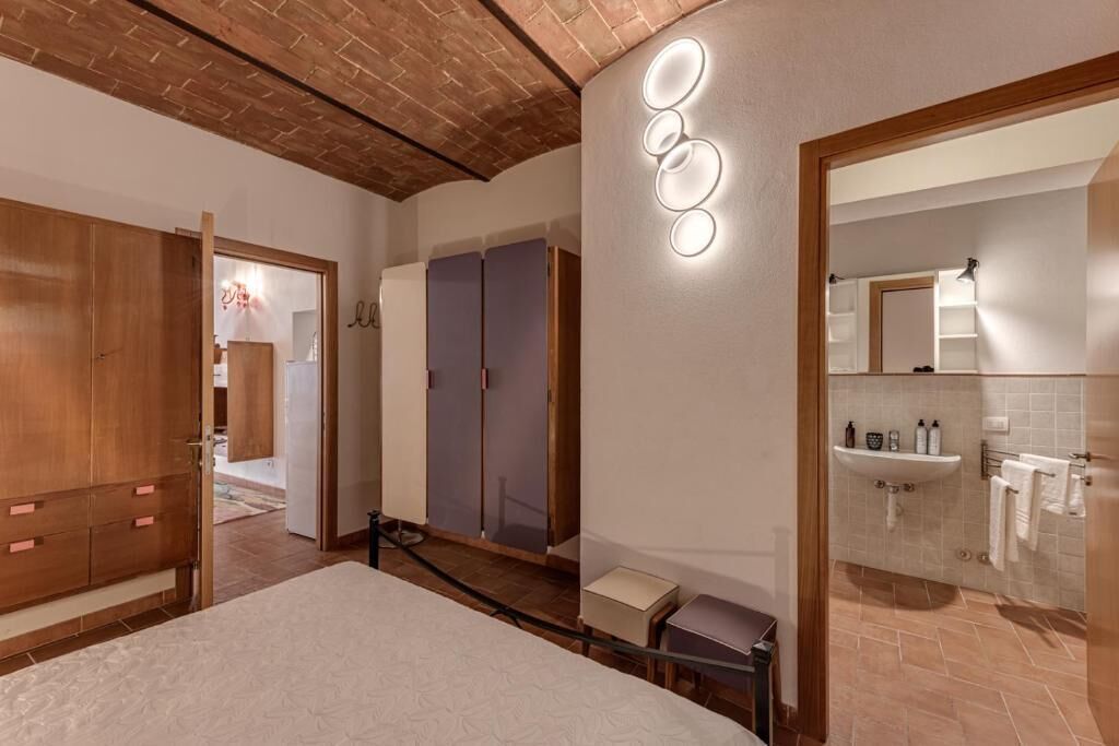 Una habitación de hotel con una cama, un armario de madera, un espejo y un baño con lavabo y toallero.