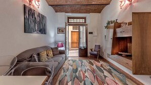 Ein gemütliches Wohnzimmer mit Backstein Decke, einer Couch, einem Sessel, einem gemusterten Teppich und einer Holzkommode.