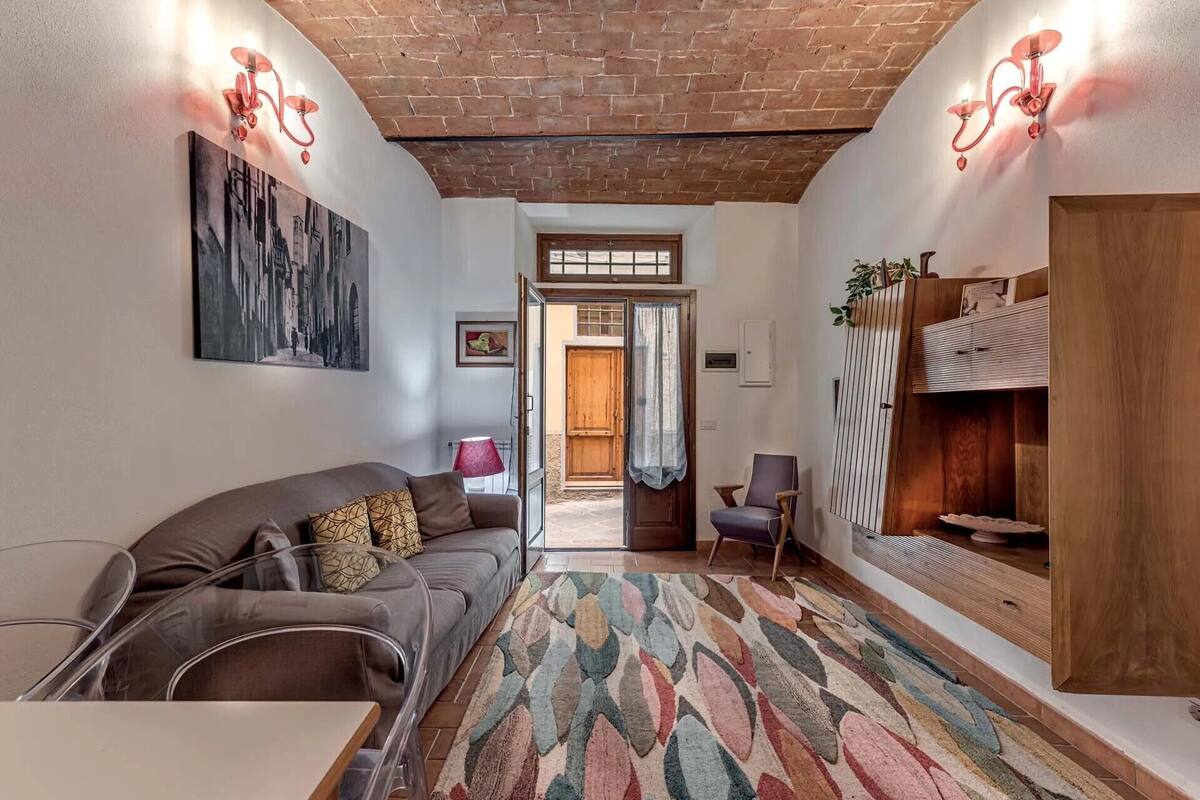 Una sala de estar acogedora con techo de ladrillo, un sofá, un sillón, un tapete estampado y un mueble de madera.