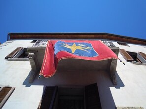 Fachada de edificio con un llamativo emblema azul y amarillo, un toldo rojo y una ventana con celosía decorativa.