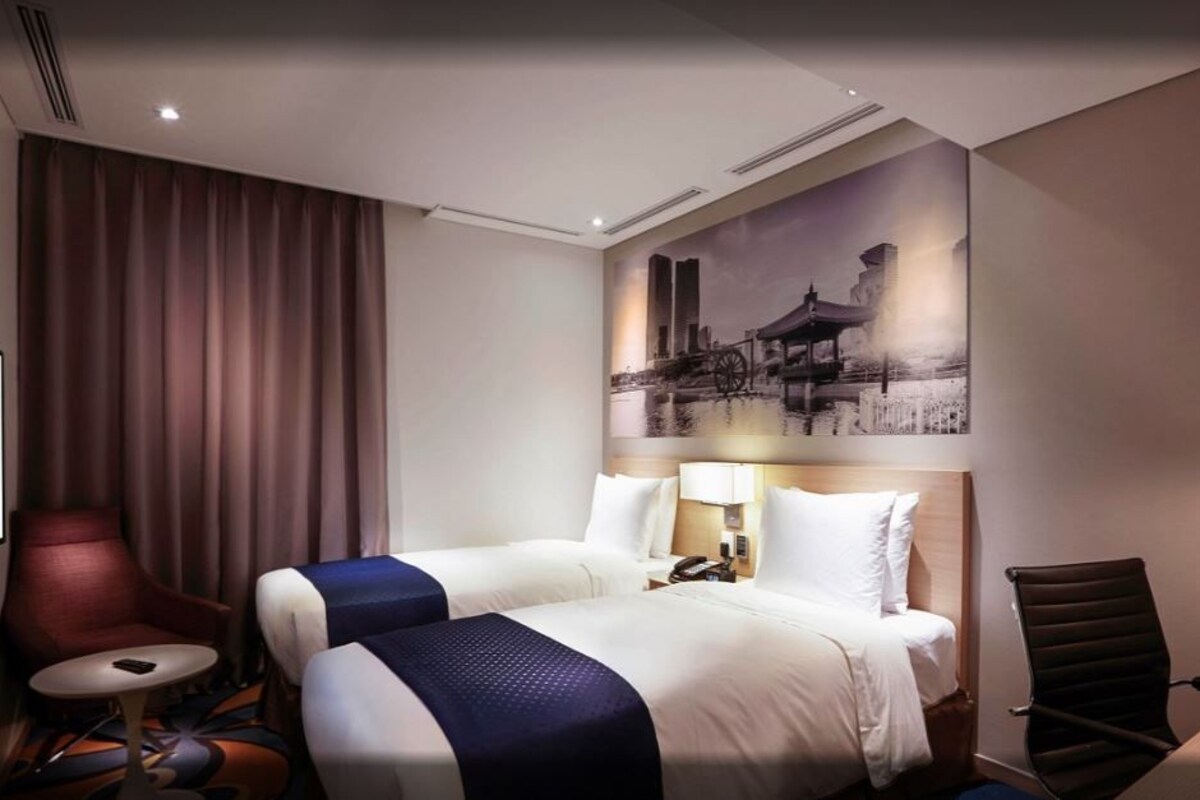 A hotel room with two beds, a desk, a chair, a TV, and a large wall mural.