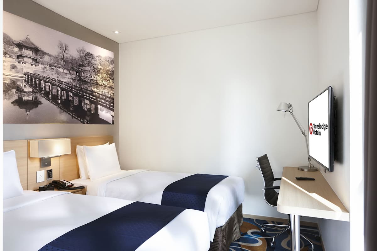 Une chambre d’hôtel avec deux lits, une télévision, un bureau et un grand tableau accroché au mur.