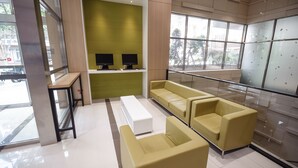 A modern waiting area with a sofa, a bench, and two monitors on a shelf.