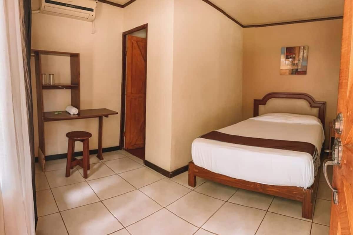 Un dormitorio con una cama, un escritorio de madera, un taburete y una puerta.