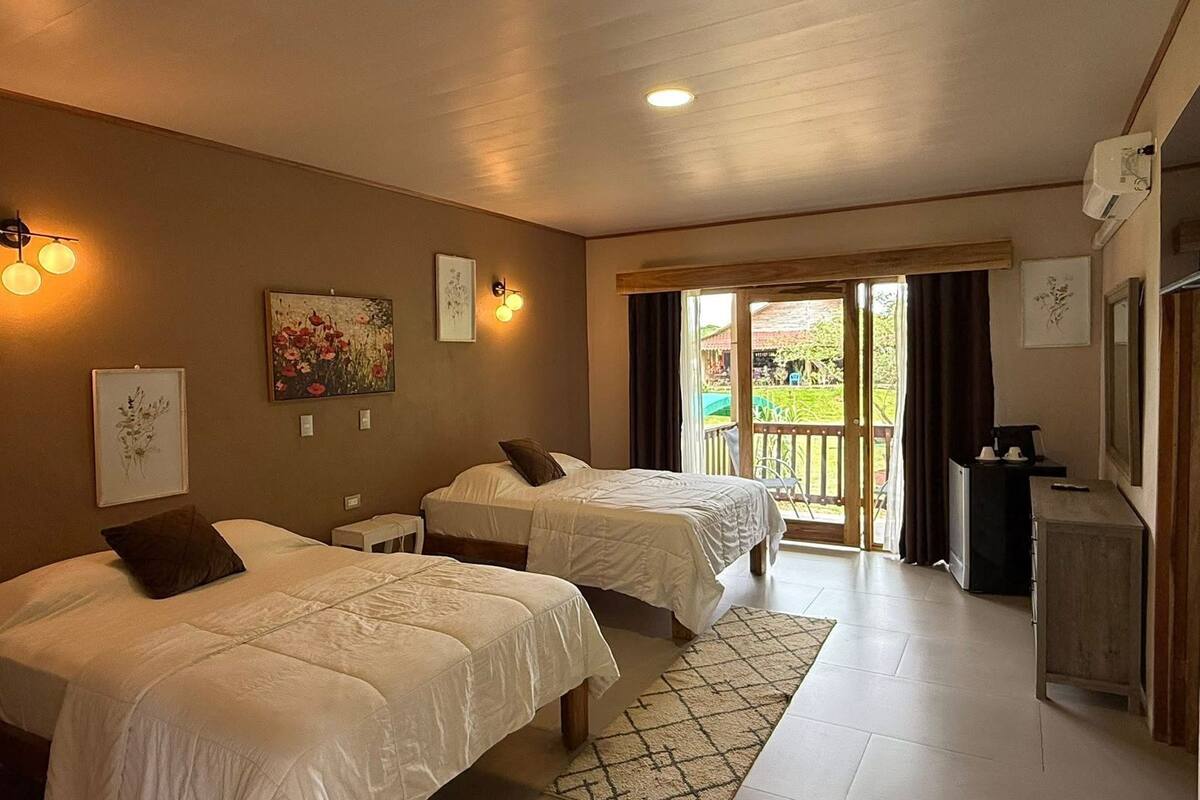 Habitación de hotel con dos camas, una mesita, una silla, un escritorio y un balcón con vistas.