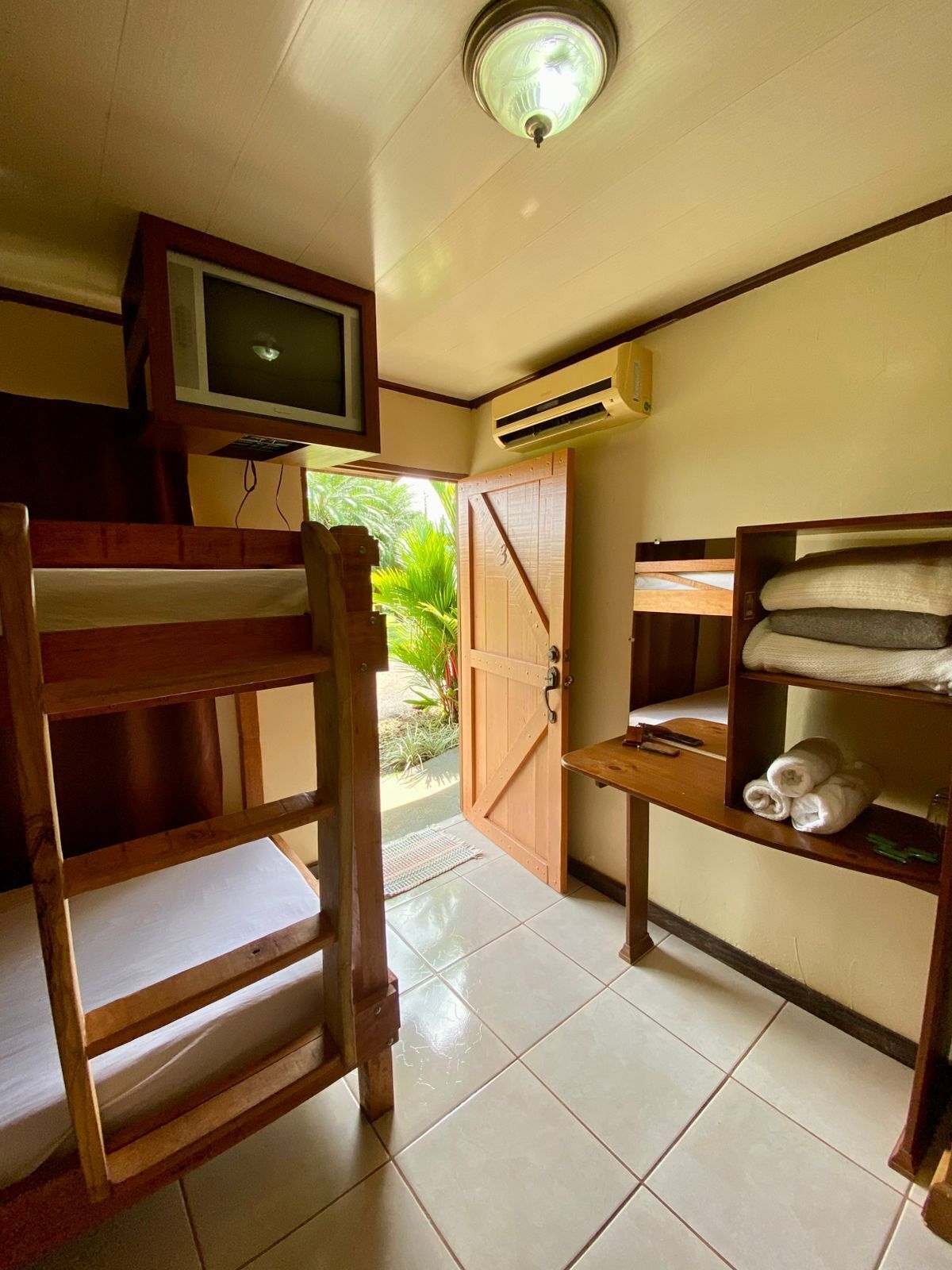 Une chambre équipée d’un lit superposé, d’une télévision, d’un climatiseur et d’une étagère avec des serviettes.