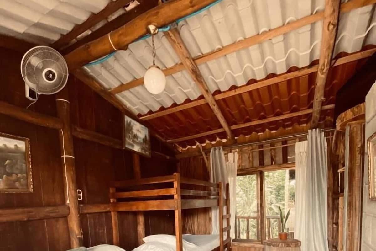 Una cabaña rústica con dos literas, un ventilador, una ventana con cortinas y una alfombra estampada.