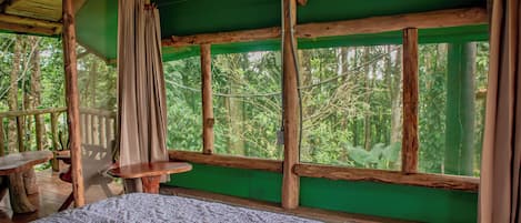 A room with a bed, a table, and a view of the forest.