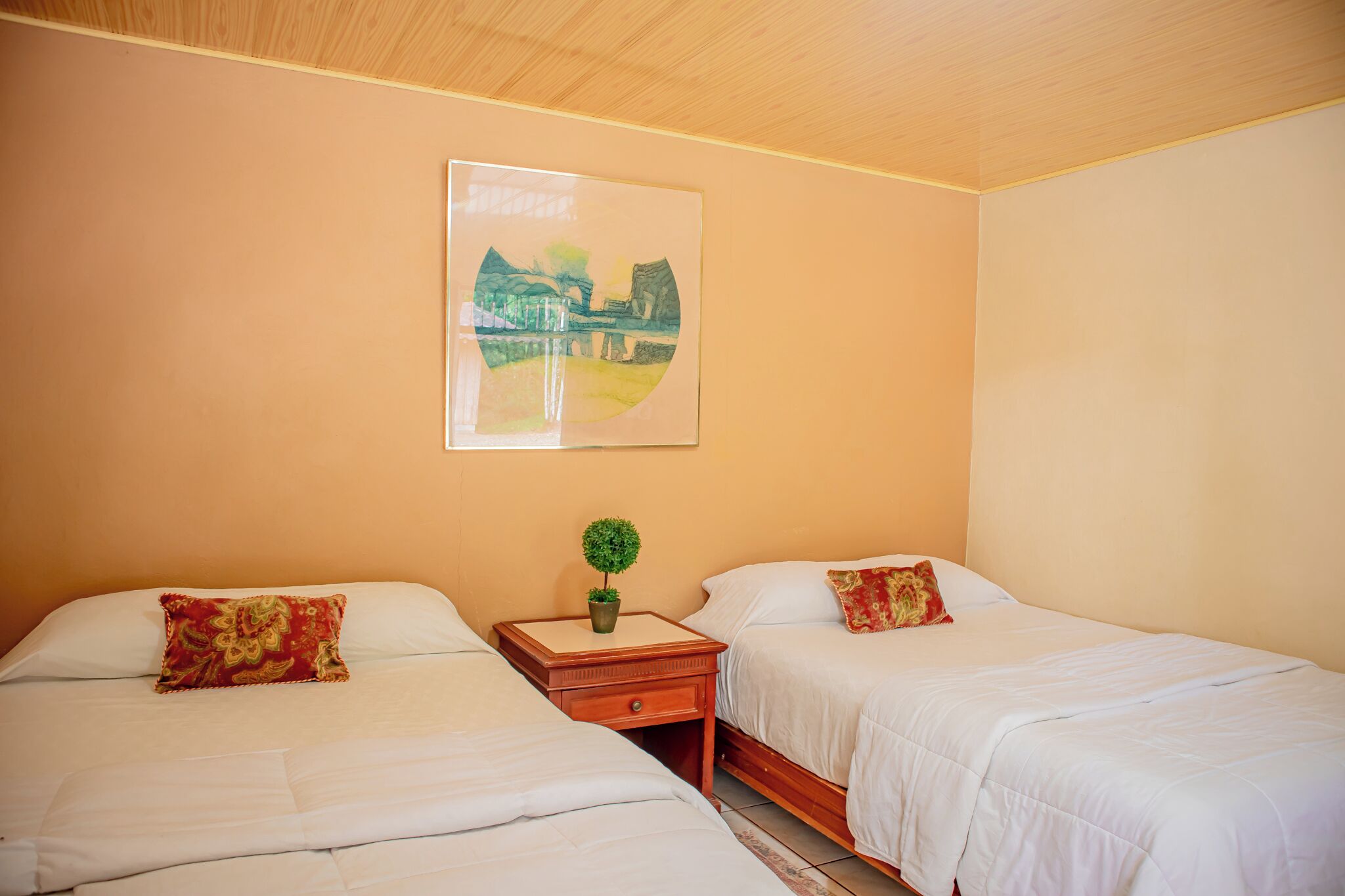 A hotel room with two beds, a nightstand with a plant, and a painting on the wall.