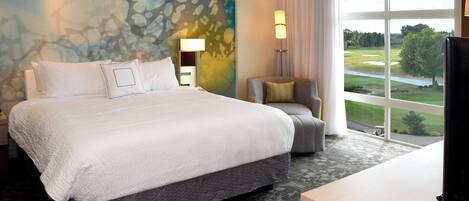 A hotel room with a large bed, a desk, and a view of a golf course.