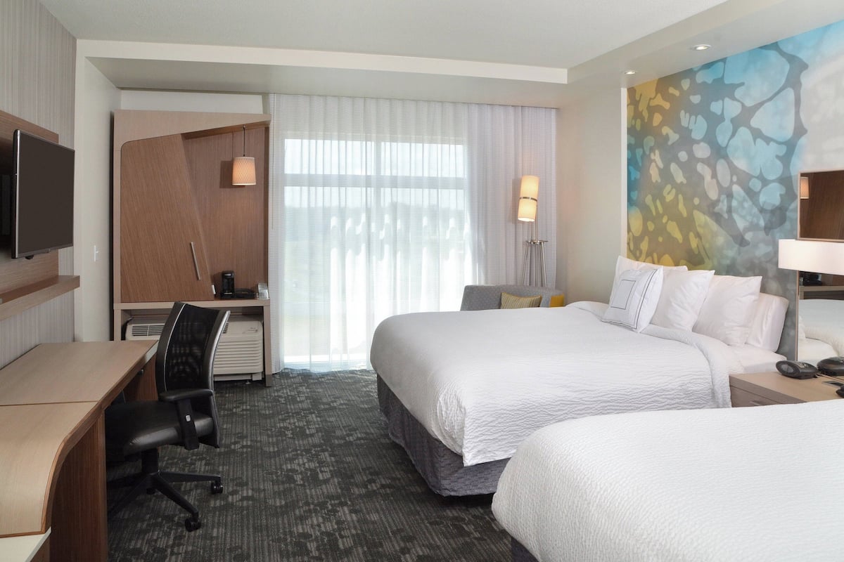 Ein Hotelzimmer mit Bett, Schreibtisch, Stuhl, Fernseher und Bildern an der Wand.