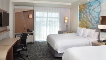 A hotel room with a bed, desk, chair, TV, and artwork on the wall.
