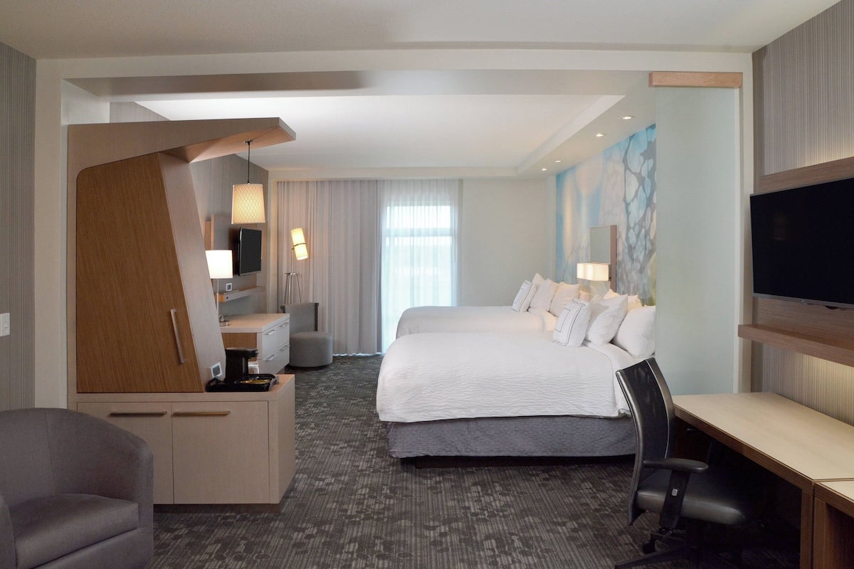 Ein Hotelzimmer mit Bett, Schreibtisch, Stuhl, Fernseher und einem Kunstwerk an der Wand.