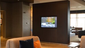 A modern hotel lobby with a flat-screen TV displaying a scenic waterfall, comfortable seating with patterned cushions, and a clean, contemporary design. - Courtyard by Marriott Youngstown Canfield (Canfield)