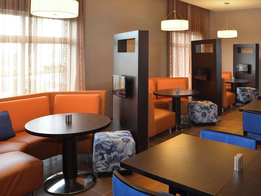 A hotel lobby with orange seating, round tables, and a TV on a wooden panel.