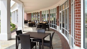 An outdoor patio area with a curved brick wall, large windows, and a seating area with tables and chairs. - Courtyard by Marriott Youngstown Canfield (Canfield)