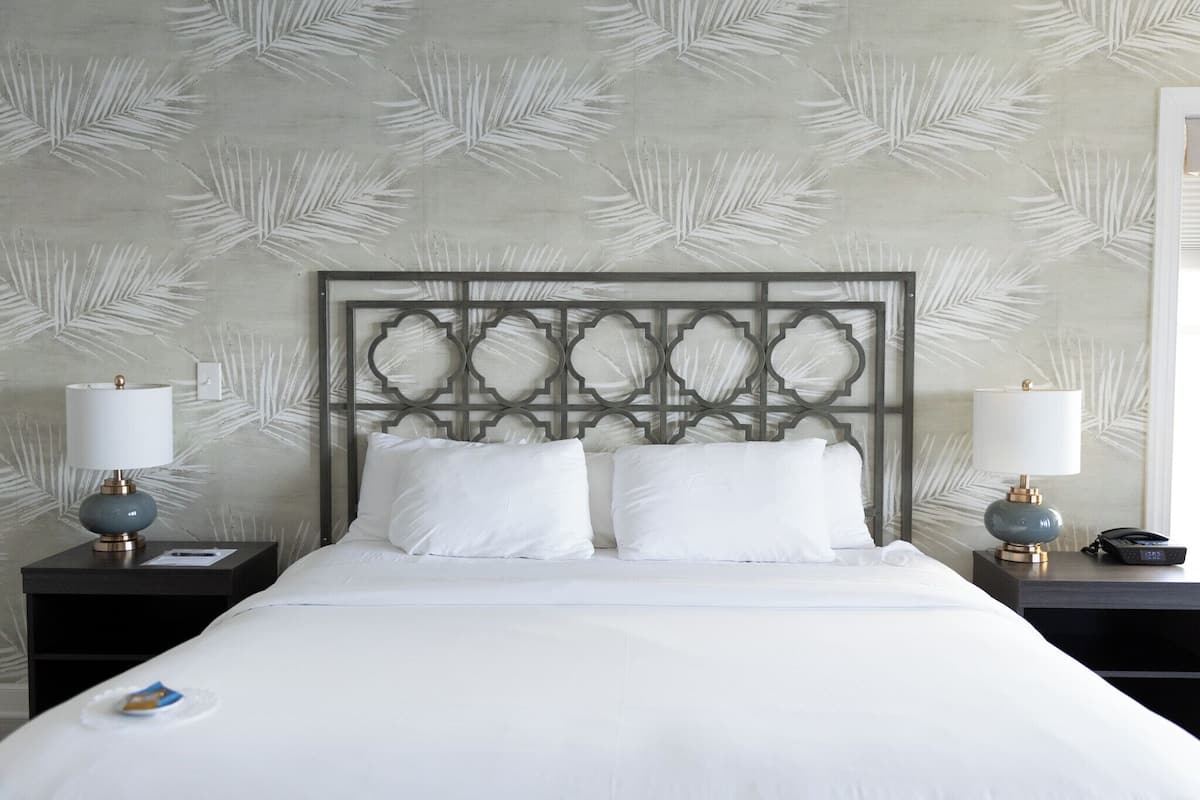 A neatly made bed with white linens, two bedside tables with lamps, and a patterned wall.