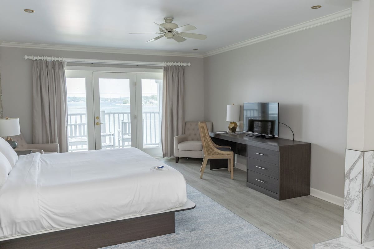A hotel room with a large bed, a desk with a television, a chair, and a view of the outdoors through a sliding door.