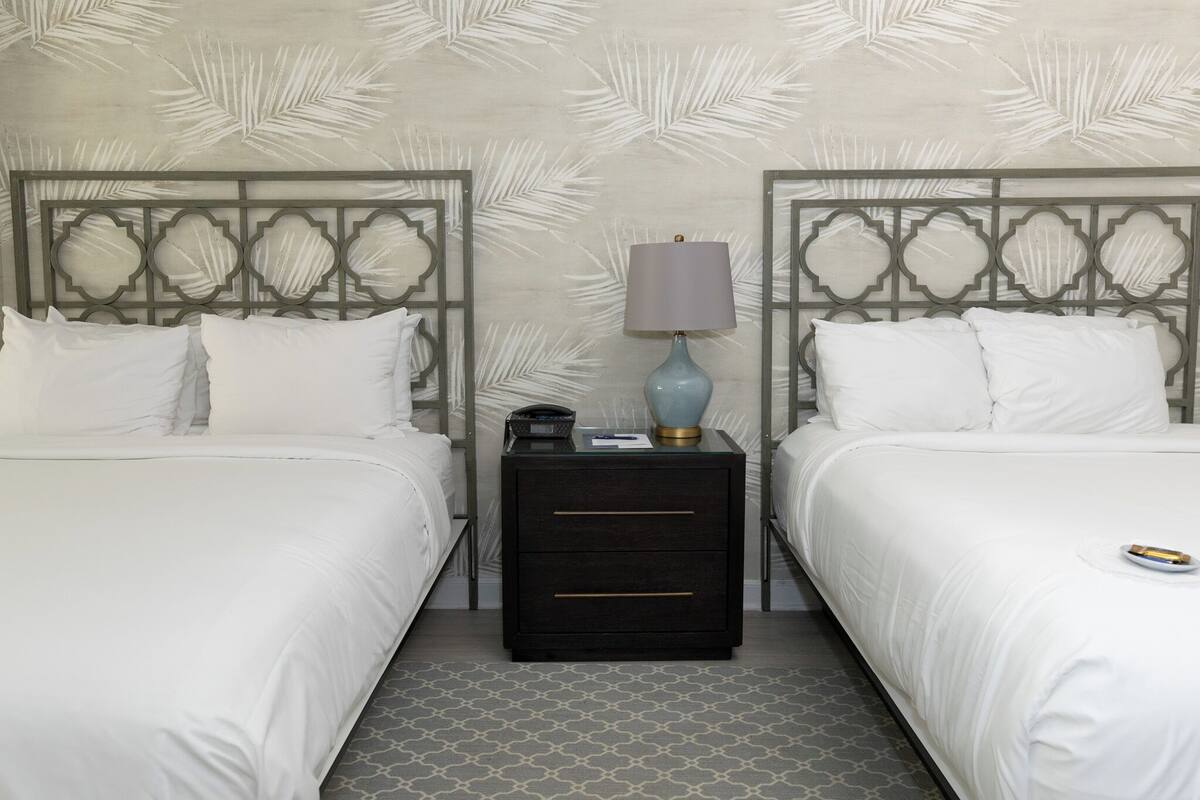 A hotel room with two beds, a nightstand with a lamp, and a patterned wall.
