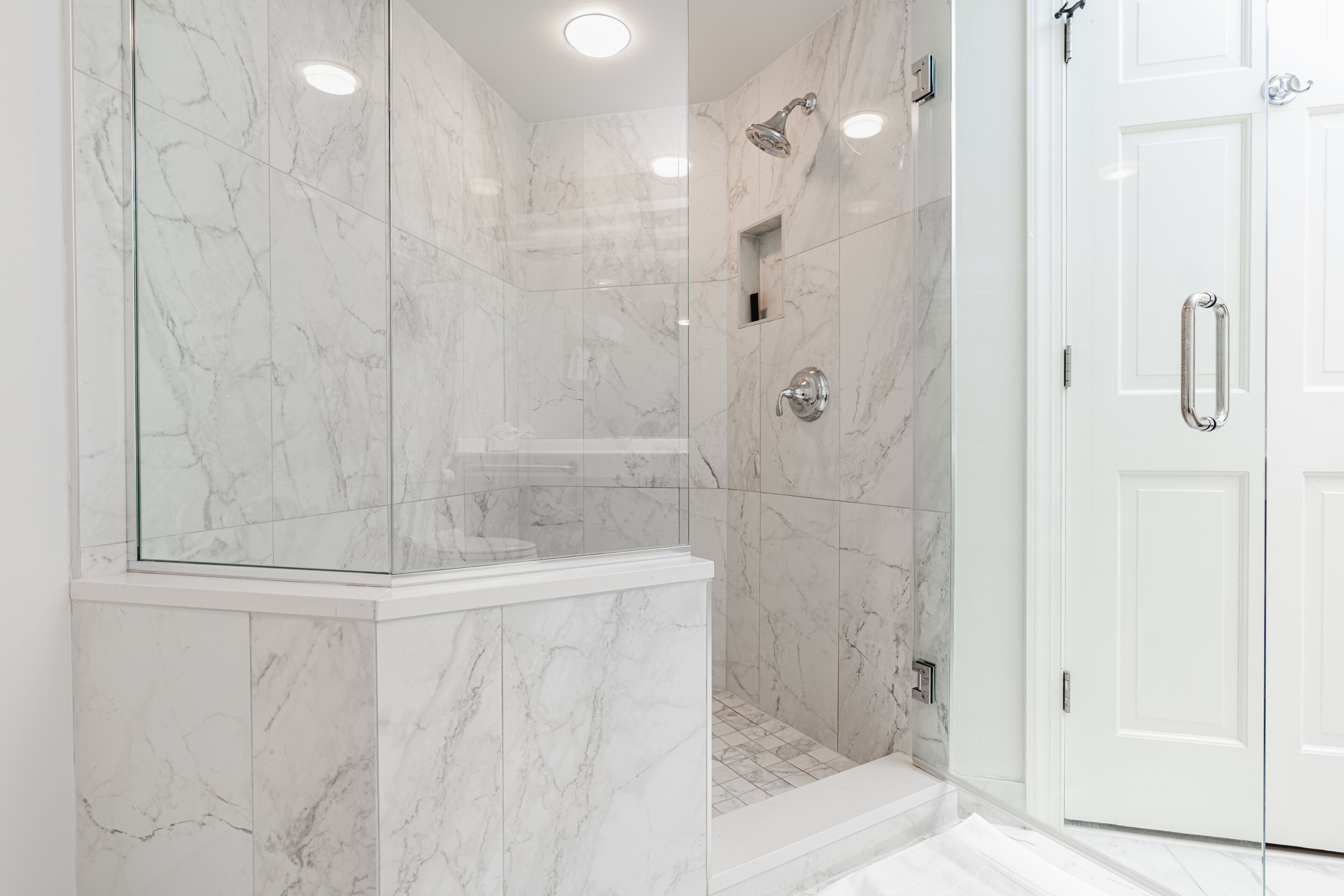 A modern bathroom with marble walls, a glass-enclosed shower, and a white door.