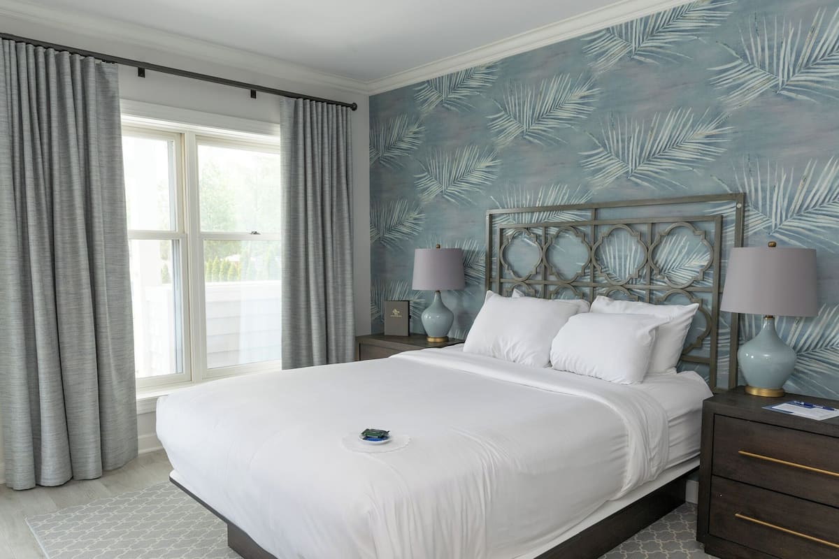 A neatly made bed with white linens, a nightstand with a lamp, and a wall with a leaf pattern.