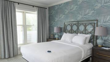 Uma cama bem arrumada com lençóis brancos, uma mesa de cabeceira com abajur e uma parede com padrão de folhas.