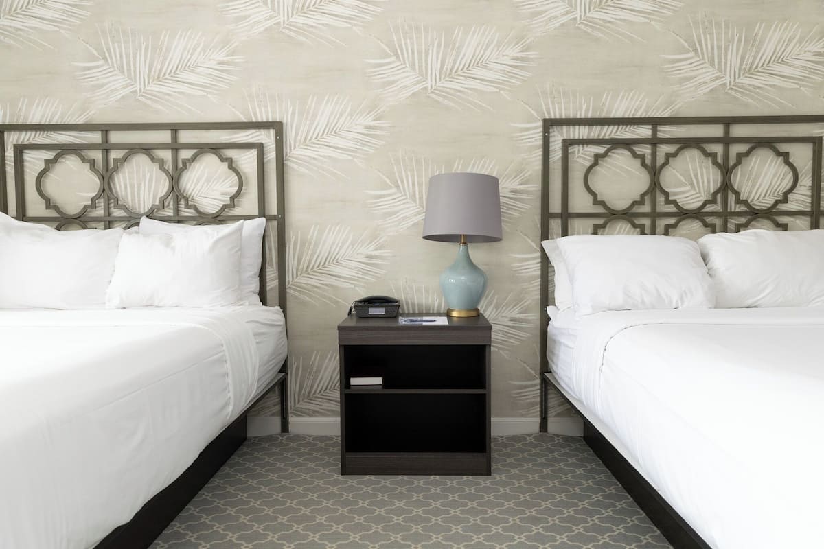 A hotel room with two beds, a nightstand with a lamp, and a patterned wall.