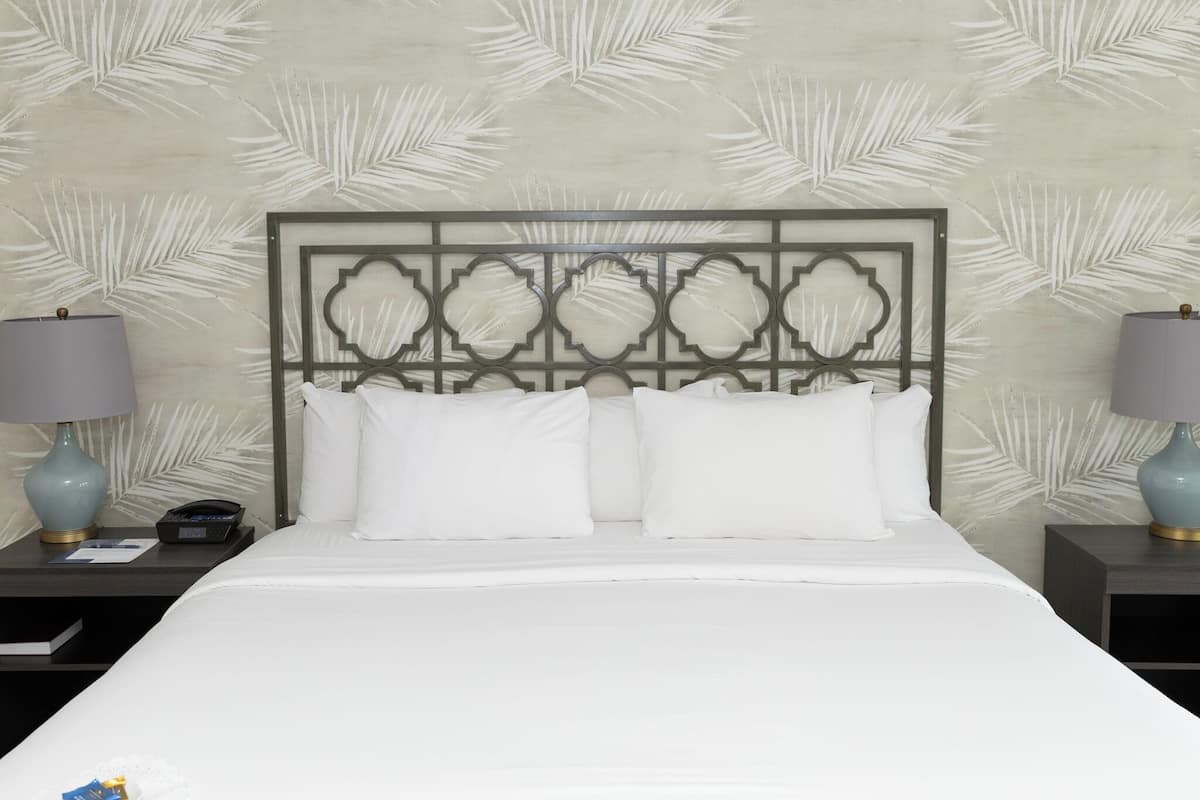 A neatly made bed with a decorative headboard, two bedside tables with lamps, and a patterned wall.