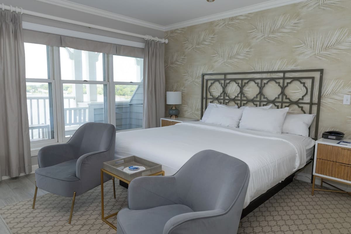 A hotel room with a large bed, two armchairs, a small table, and a nightstand.