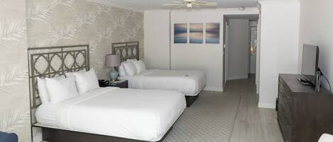 A hotel room with two beds, a ceiling fan, a TV, and a dresser.