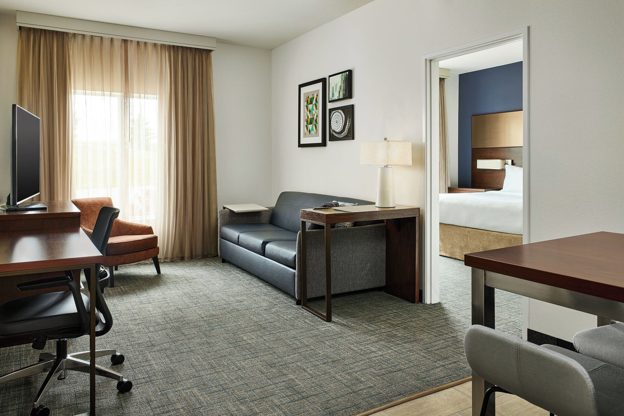 A hotel room with a desk, a sofa, a TV, and a bed.