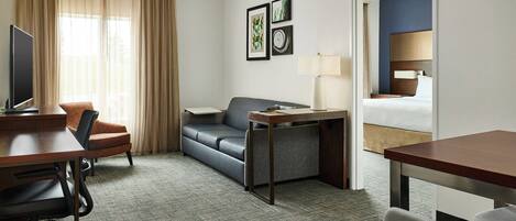 A hotel room with a desk, a sofa, a TV, and a bed.
