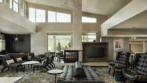 A spacious lounge area with a fireplace, comfortable seating, and large windows providing natural light. - Residence Inn Rapid City (Rapid City)