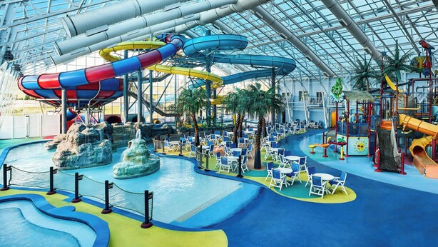 An indoor water park with multiple slides and pools, surrounded by seating areas and palm trees. - Residence Inn Rapid City (Rapid City)