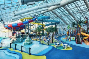 Parque acuático interior con múltiples toboganes y piscinas, rodeado de zonas de descanso y palmeras.