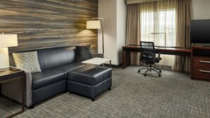 A hotel room with a black leather sofa, a small table, a desk with a chair, a TV, and a large window with curtains. - Residence Inn Rapid City (Rapid City)