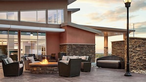 An outdoor patio area with wicker furniture, a stone fire pit, and a modern building with large windows and a stone wall. - Residence Inn Rapid City (Rapid City)