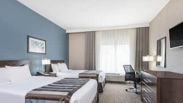 A hotel room with two beds, a desk, a chair, a TV, and a large window with curtains.